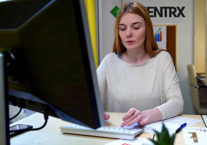 A woman in a white sweater typing at her workstation, she has very long red hair and she looks very attractive