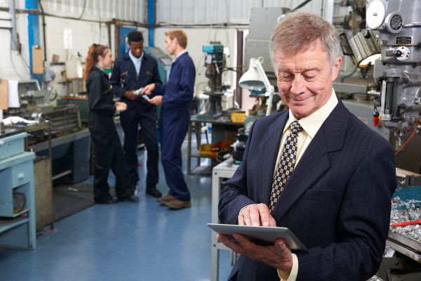 Owner Of Engineering Factory Using Digital Tablet With Staff In Background